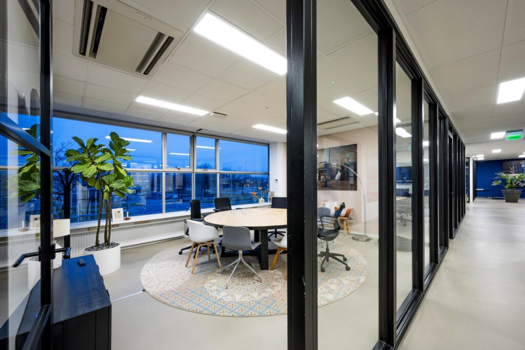 Moderne vergaderruimte aan de Van der Madeweg met glazen wanden, ronde tafel en uitzicht op de straat.